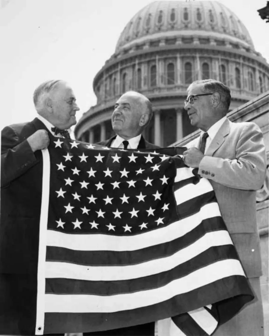 Alaska's senators hold up a 49-star flag in front of the US Capitol, late 1958 or early 1959.