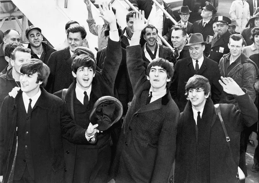 The Beatles wave to fans after arriving at New York's Kennedy Airport, 7 February 1964.