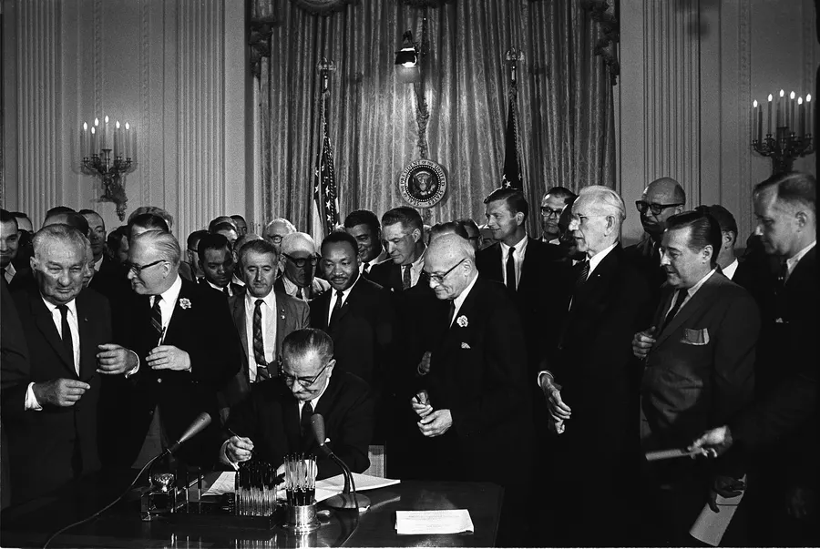 President Lyndon Johnson signs the Civil Rights Act in the White House on 2 July 1964, with Martin Luther King Jr among those looking on
