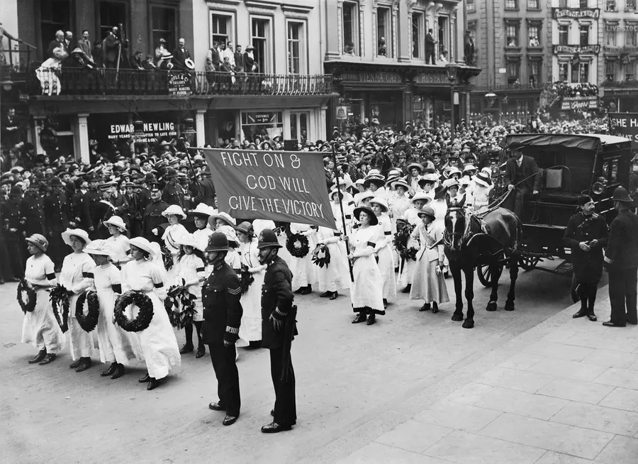 Suffragettes in white, carrying wreaths and a banner, walk in Emily Davison's funeral procession, June 1913