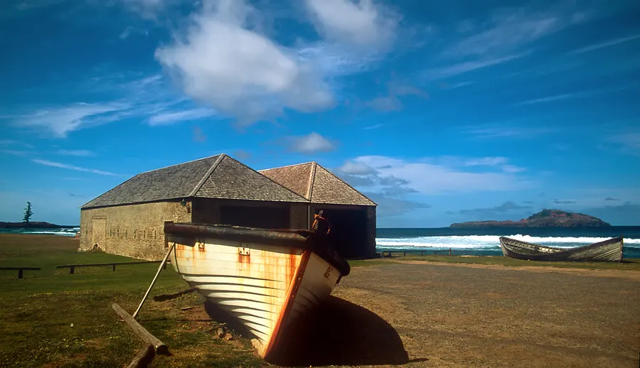 Old stone buildings and a boat on the shore at Kingston, Norfolk Island, where the Pitcairners landed