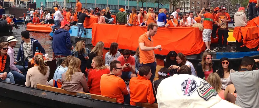 Boats full of people in orange on an Amsterdam canal on King's Day.