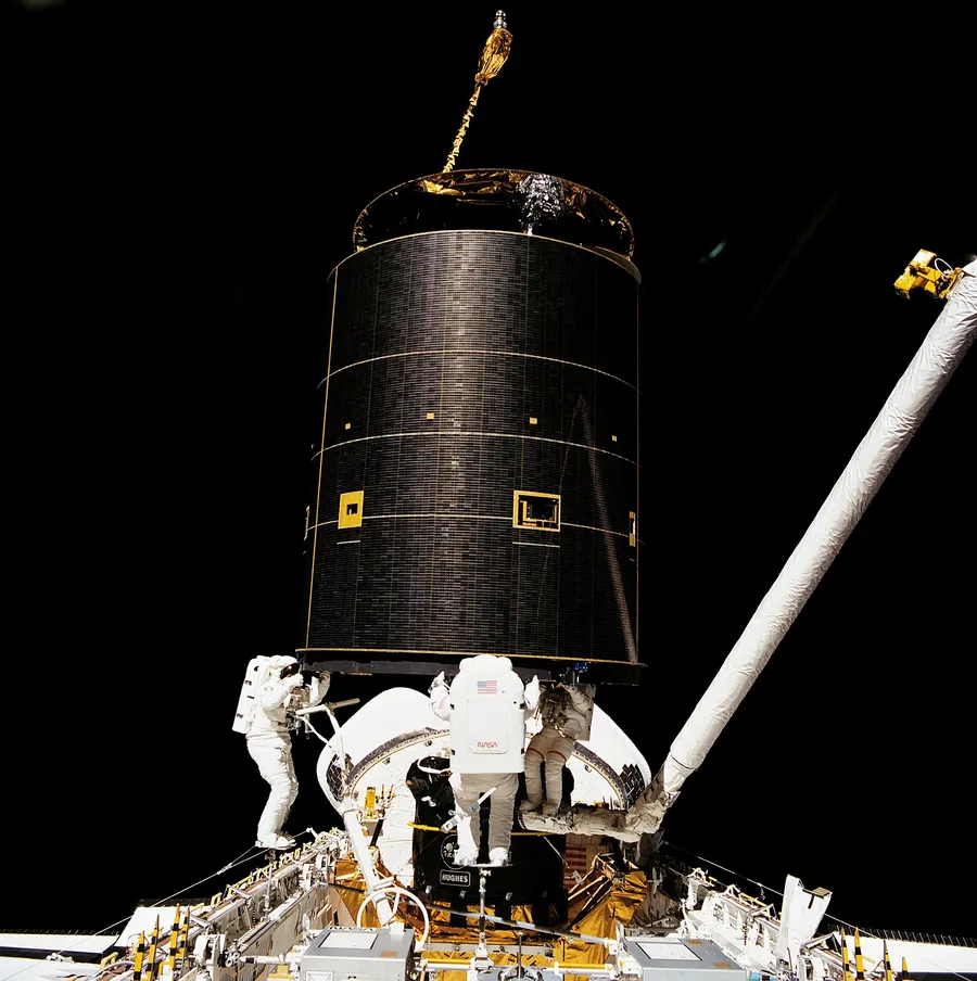 Three Endeavour astronauts hold the Intelsat VI satellite by hand during STS-49, May 1992.
